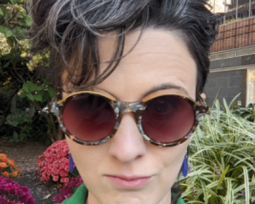 picture of Kathleen DiGiulio, a white woman with dark hair, wearing sunglasses and a green coat