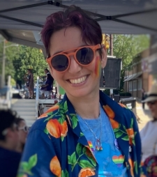white person wearing orange sunglasses, an open dark blue button down over a light blue shirt smiling