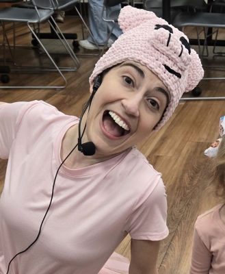 A female librarian wearing all pink with a Piggie hat and microphone