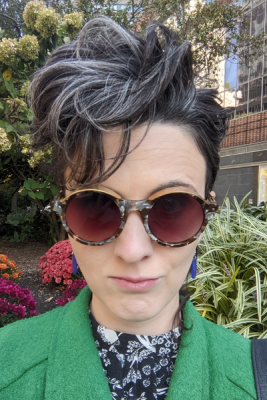 picture of Kathleen DiGiulio, a white woman with dark hair, wearing sunglasses and a green coat
