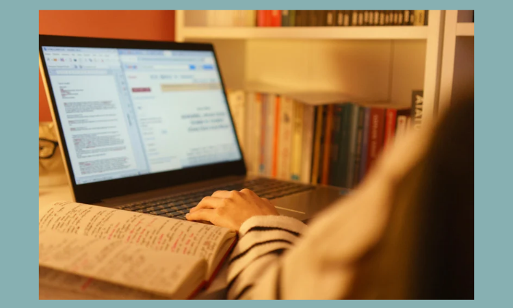 Photo of a person at a desk with a computer screen and open book.