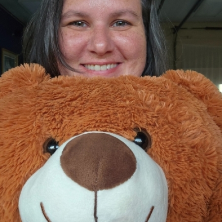 My smiling face framed by brown hair is stacked on top of a reddish-brown stuffed teddy bear's smiling face. We are story time bros.