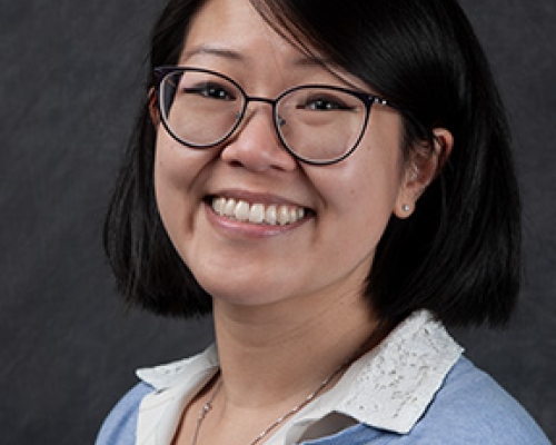 Headshot of bespectacled woman with short black hair, a white blouse and periwinkle cardigan.