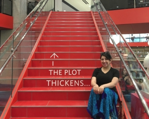 Emily is sitting on a red staircase at Boston Public Library. The text "The plot thickens..." is written on the stairs.