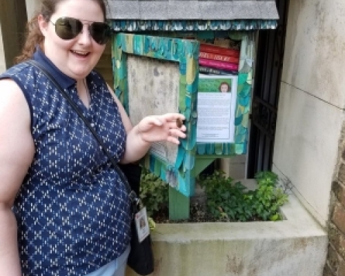 30s woman with sunglasses standing in front of a little free library