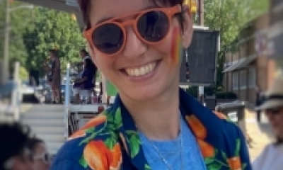 white person wearing orange sunglasses, an open dark blue button down over a light blue shirt smiling