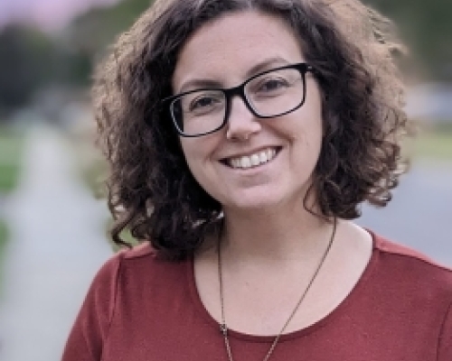 Photo of a white woman with curly hair and black glasses smiling at the camera
