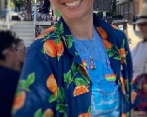 white person wearing orange sunglasses, an open dark blue button down over a light blue shirt smiling