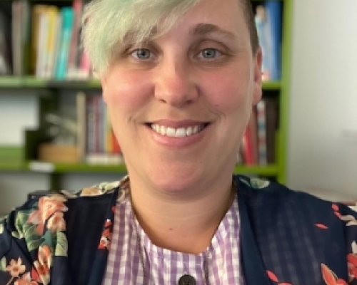 Caucasian women blue hair with bangs posing in front of shelf of books