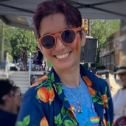 white person wearing orange sunglasses, an open dark blue button down over a light blue shirt smiling