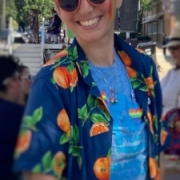 white person wearing orange sunglasses, an open dark blue button down over a light blue shirt smiling