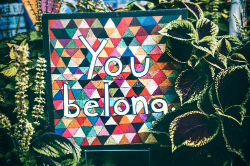 A quilt that reads "You Belong" hangs in a garden